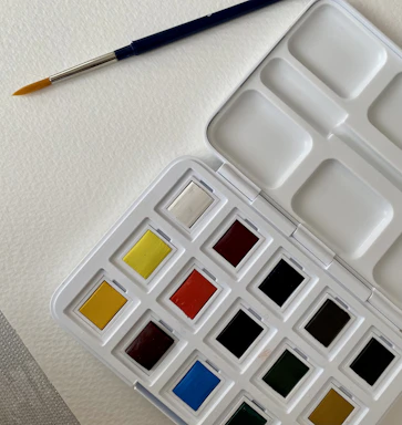 A delicate watercolor palette with brushes resting on a white table.