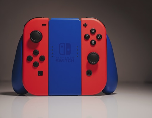 A Nintendo Switch console is set against a neutral gray background. The console features the iconic red and blue Joy-Con controllers on either side of the central blue unit, with the Nintendo Switch logo visible.