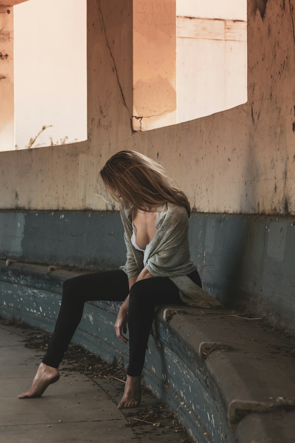 Frau in grauem Langarmhemd und schwarzer Hose sitzt auf Betonbank