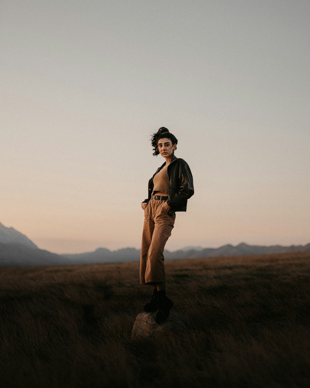 woman in brown jacket standing on brown grass field during daytime