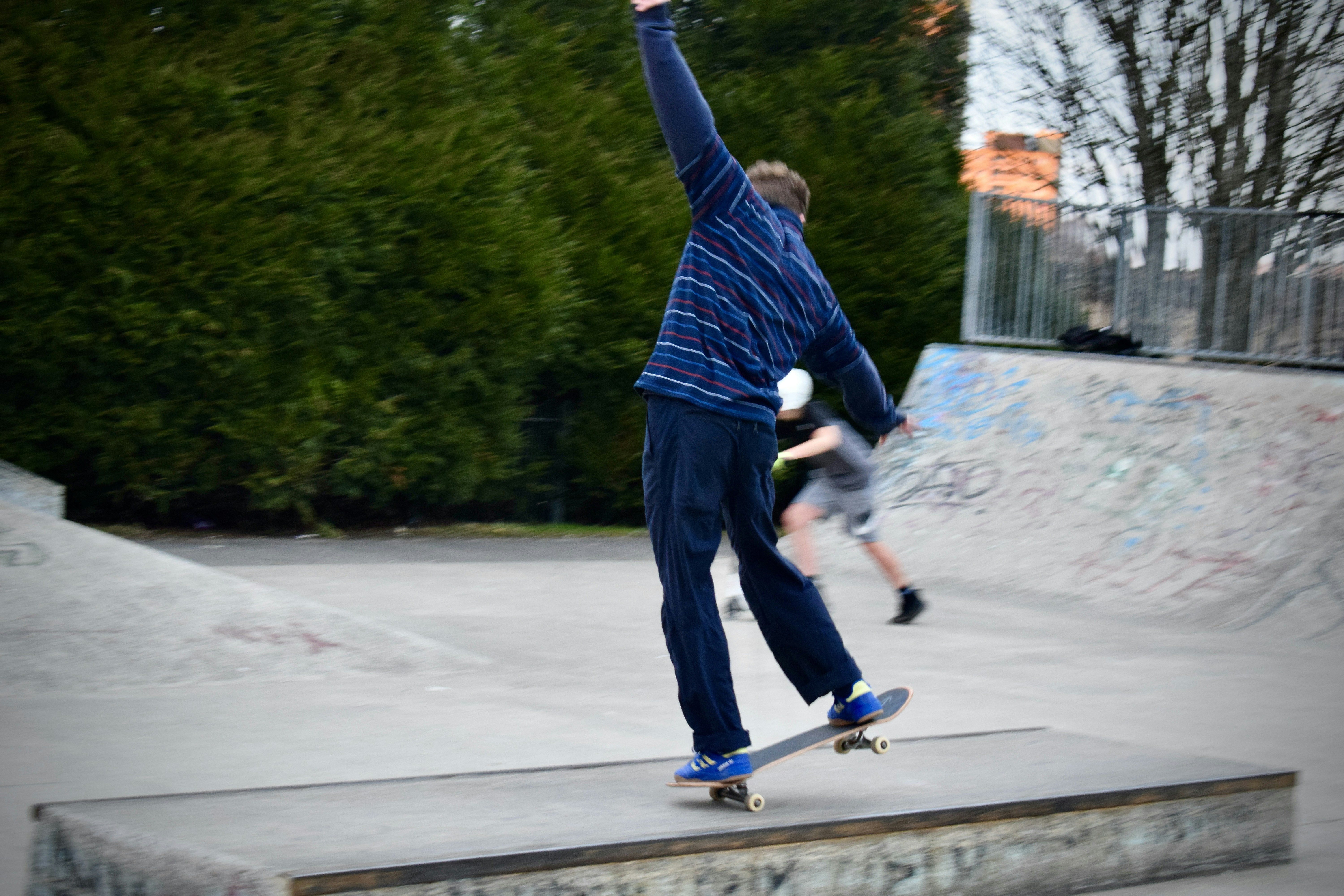 man in blue long sleeve shirt and black pants riding blue and white skateboard during daytime