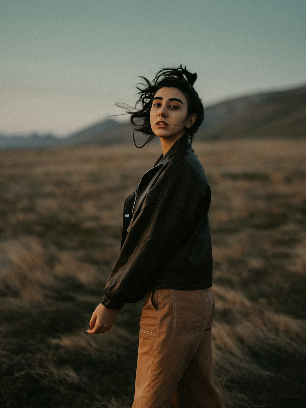 woman in black jacket and brown pants standing on brown grass field during daytime