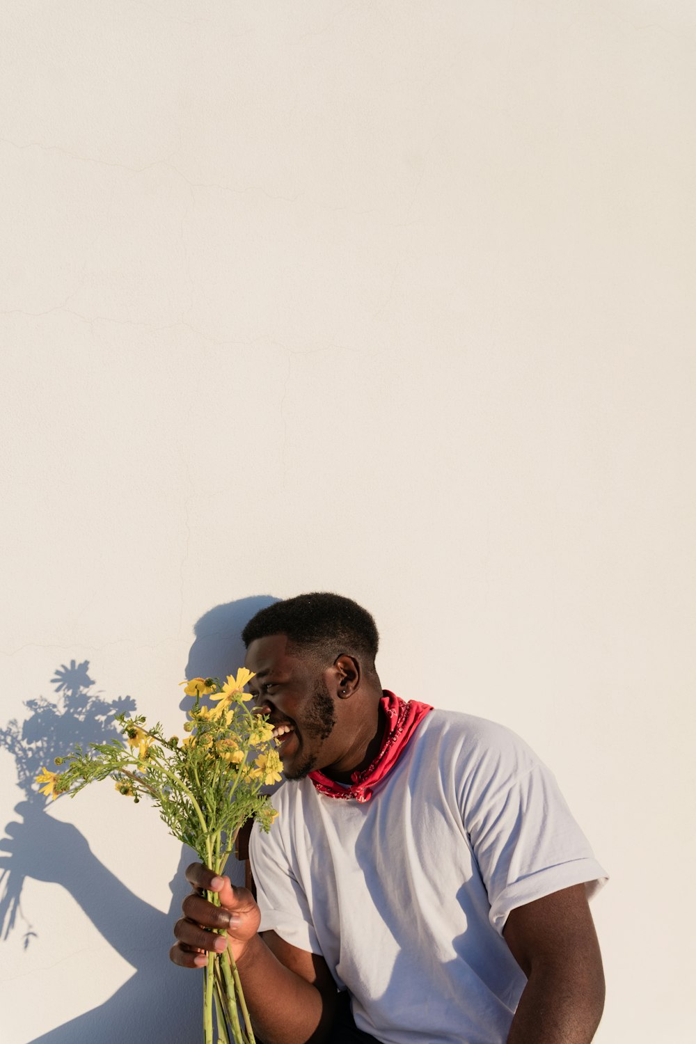 homme en t-shirt à col rond blanc tenant un bouquet de fleurs jaunes