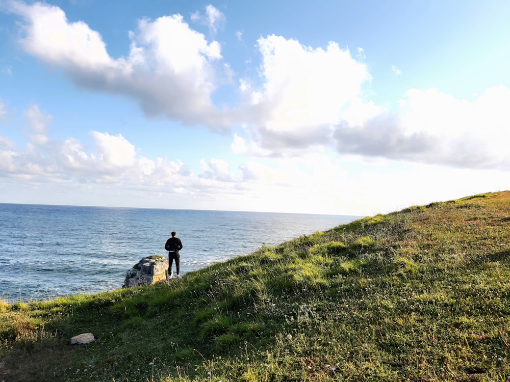 person standing on green grass field near body of water during daytime