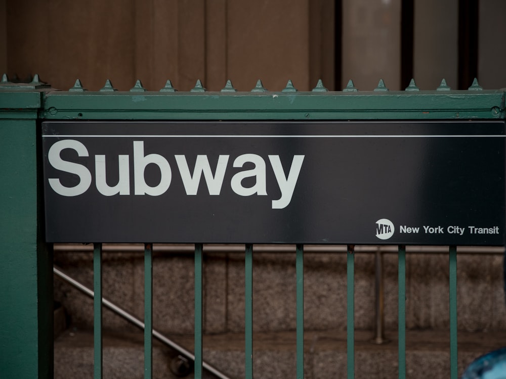 a subway sign on a green metal fence