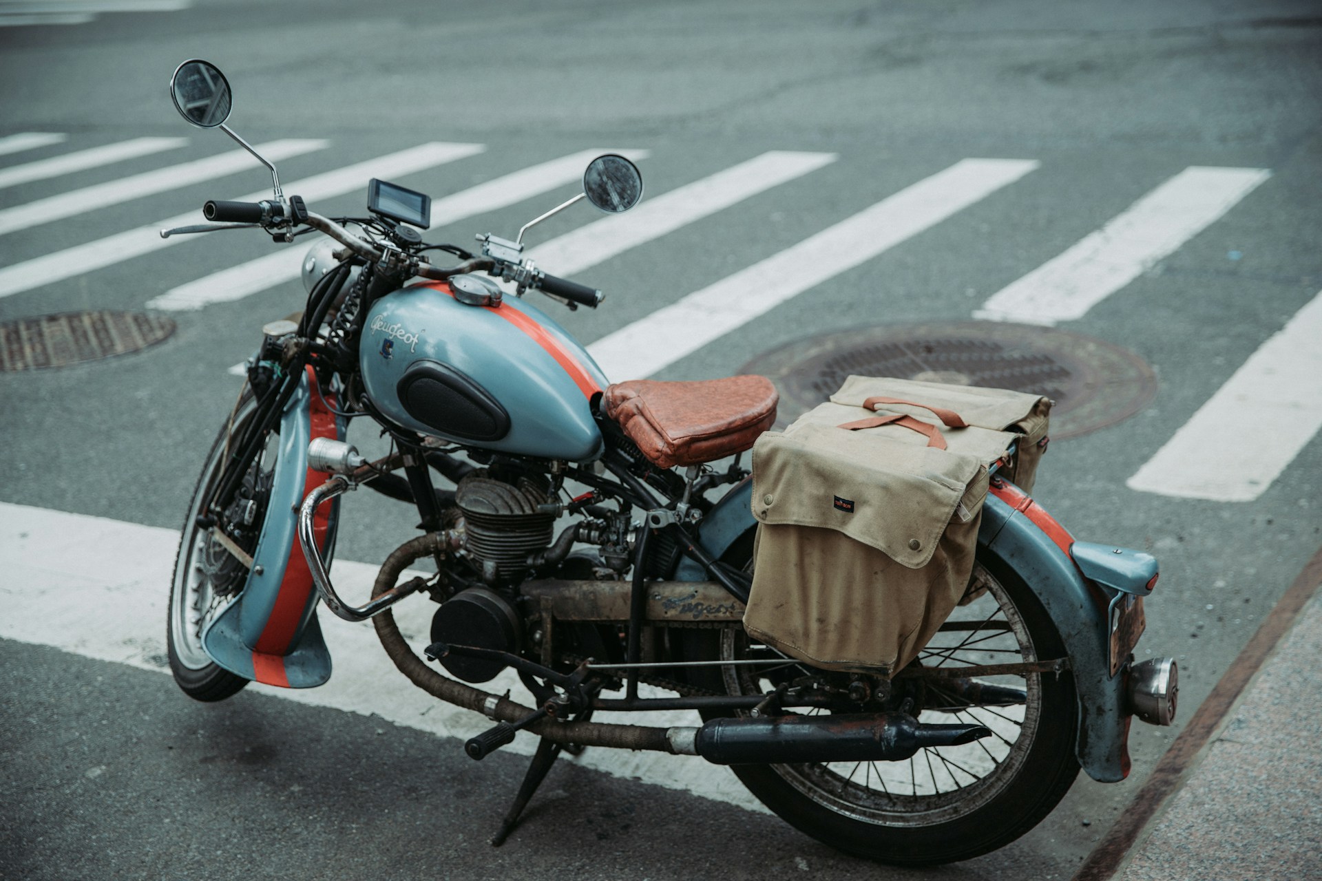 A stylish crossbody bag in deep navy blue, casually draped over a vintage bicycle handlebar on a sunny city street.