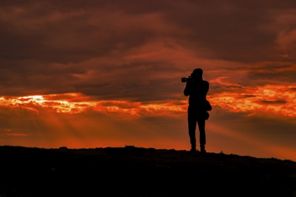 silhouette photo of man standing on hill during sunset
