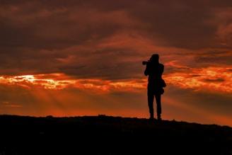 silhouette photo of man standing on hill during sunset