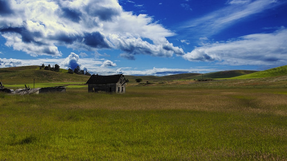 casa di legno marrone sul campo di erba verde sotto il cielo nuvoloso blu e bianco durante il giorno