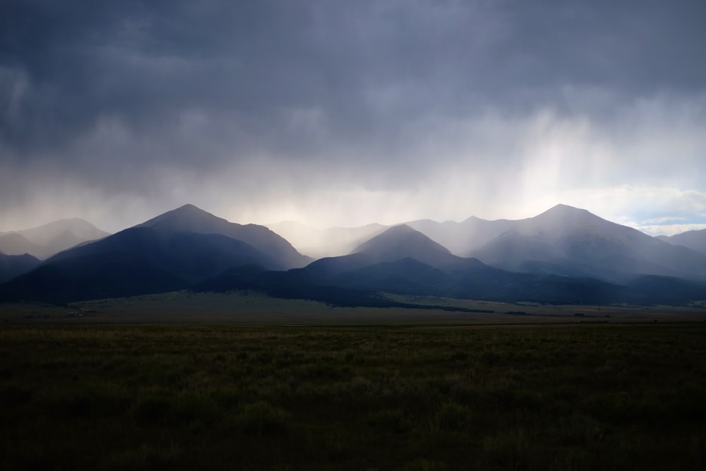 green grass field near mountain under white clouds during daytime