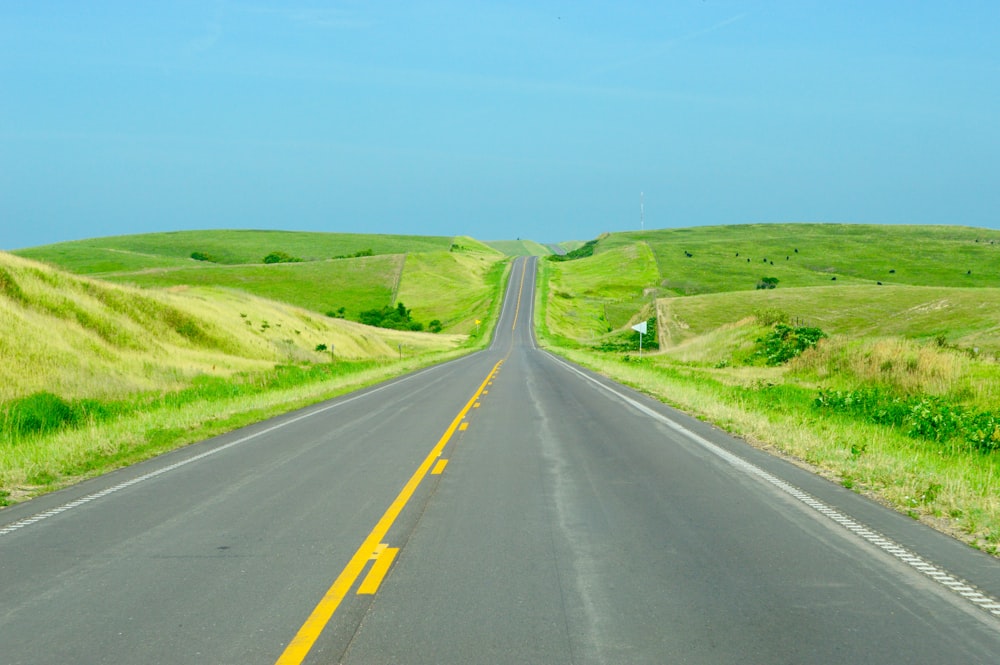 gray concrete road between green grass field under blue sky during daytime