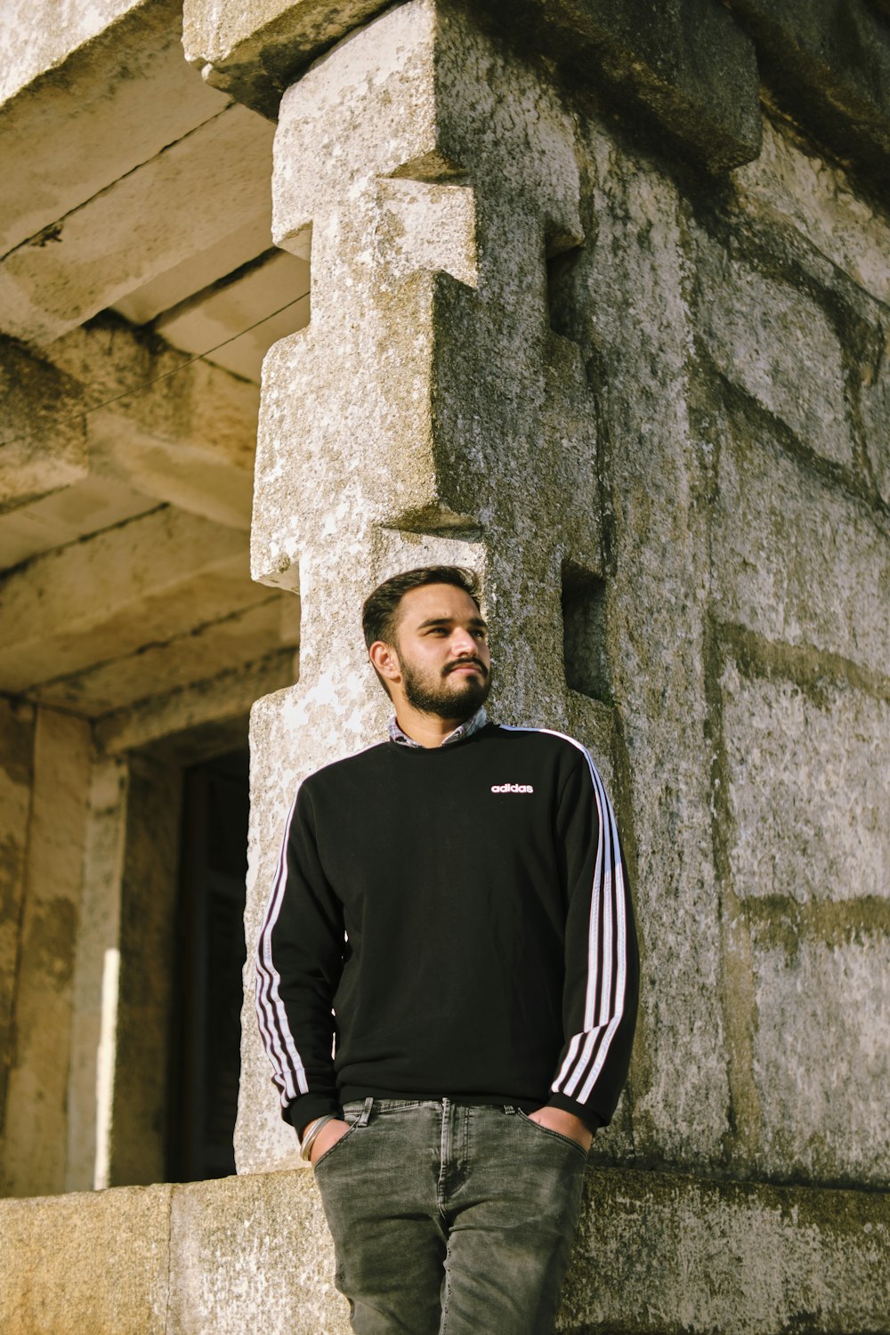 man in black crew neck shirt and black and white track jacket standing beside gray concrete