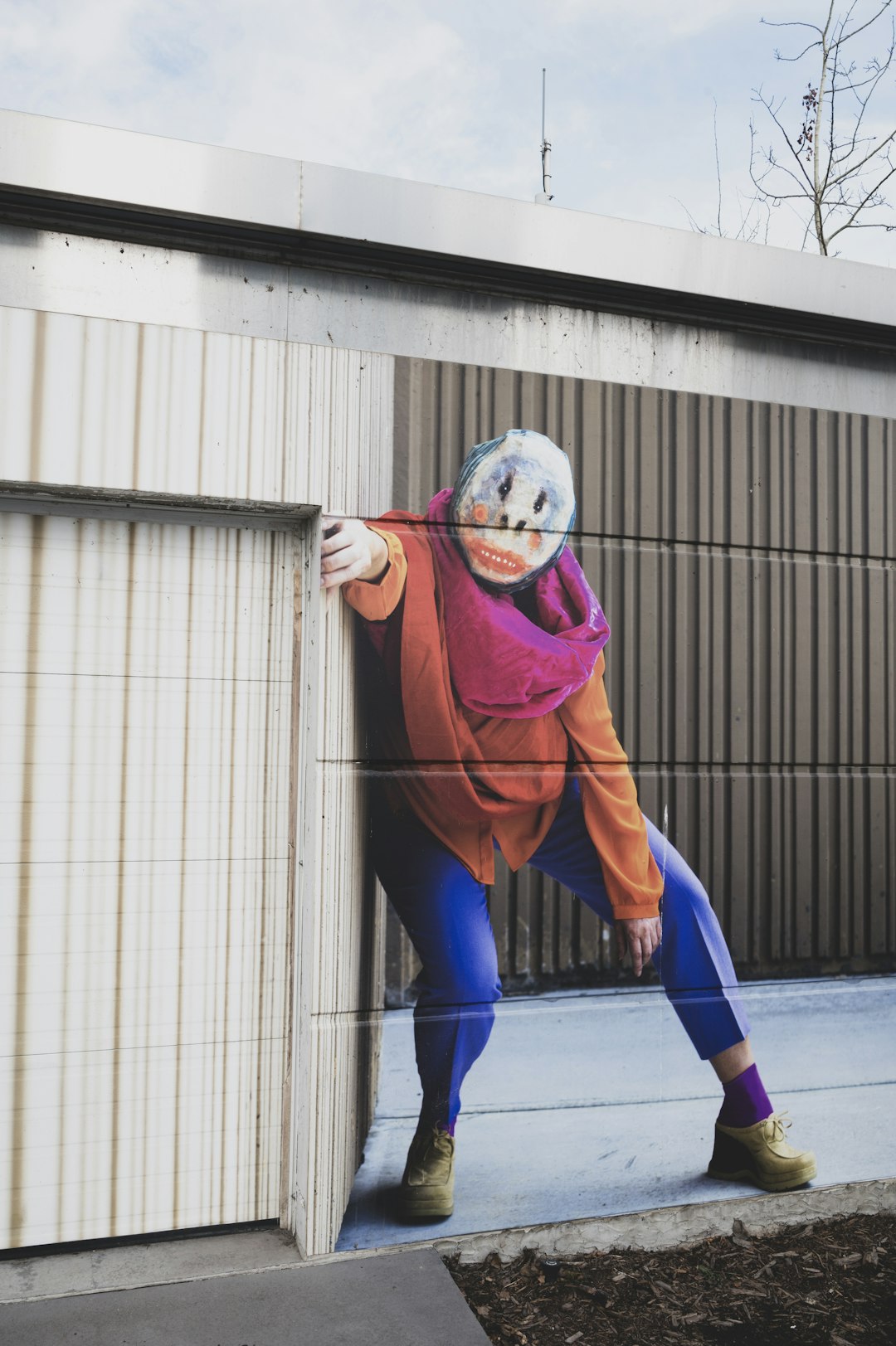 man in blue pants wearing mask standing beside brown wall