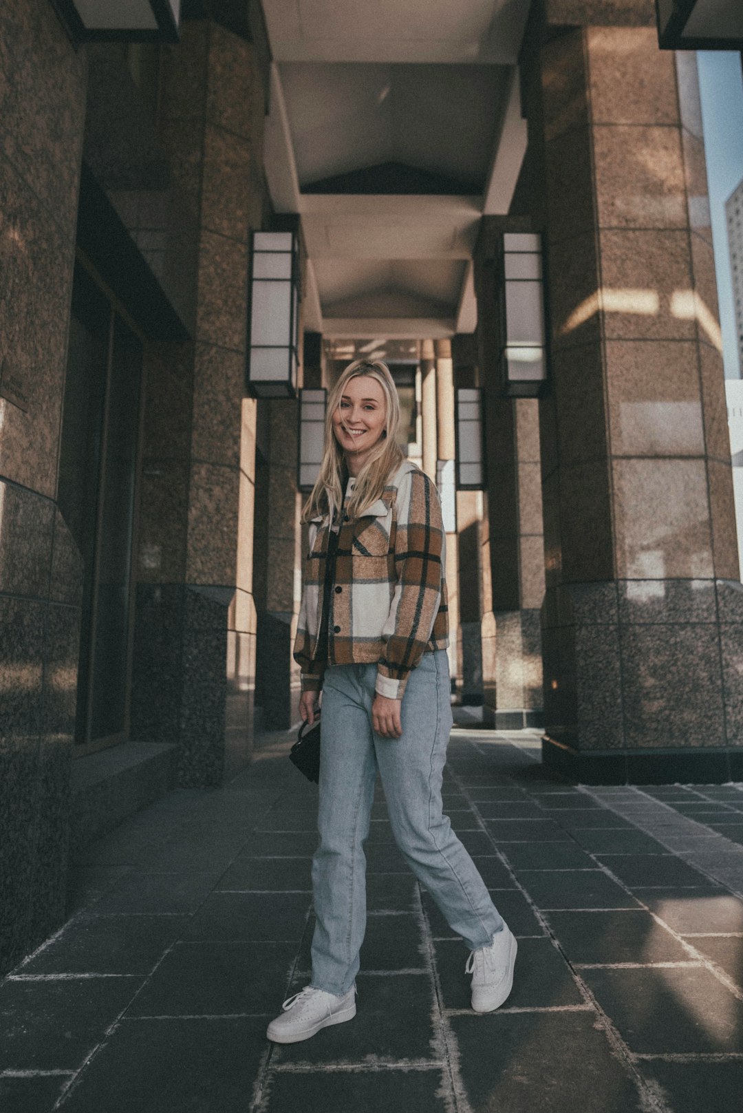 woman in brown and white plaid scarf standing beside brown brick wall