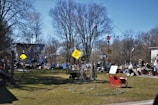 A cluttered outdoor space filled with various objects, including signs, a red sleigh, a ladder, and different piles of materials. A house with a metal roof is in the background, surrounded by leafless trees. The scene appears disorganized with numerous items scattered across the yard.