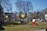 A cluttered outdoor space filled with various objects, including signs, a red sleigh, a ladder, and different piles of materials. A house with a metal roof is in the background, surrounded by leafless trees. The scene appears disorganized with numerous items scattered across the yard.
