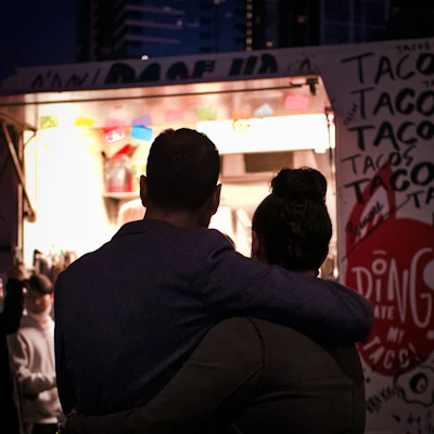 Happy customers enjoying tacos at a lively outdoor food truck event under string lights.
