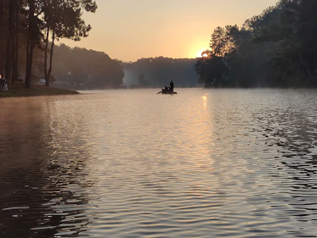 A serene scene of a young person meditating by a calm lake at sunrise.