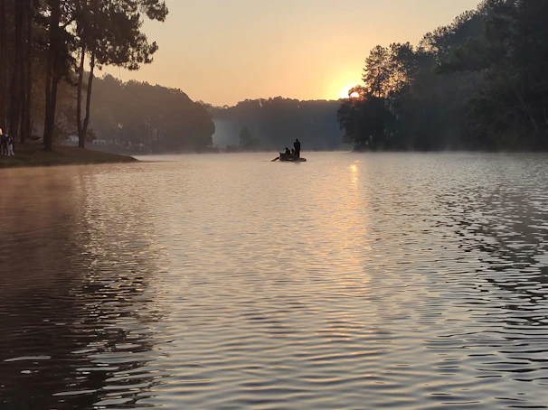 A serene morning on the lake with a boat gently cutting through calm waters and mist rising.