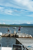 man in white t-shirt and black pants standing on brown wooden dock during daytime