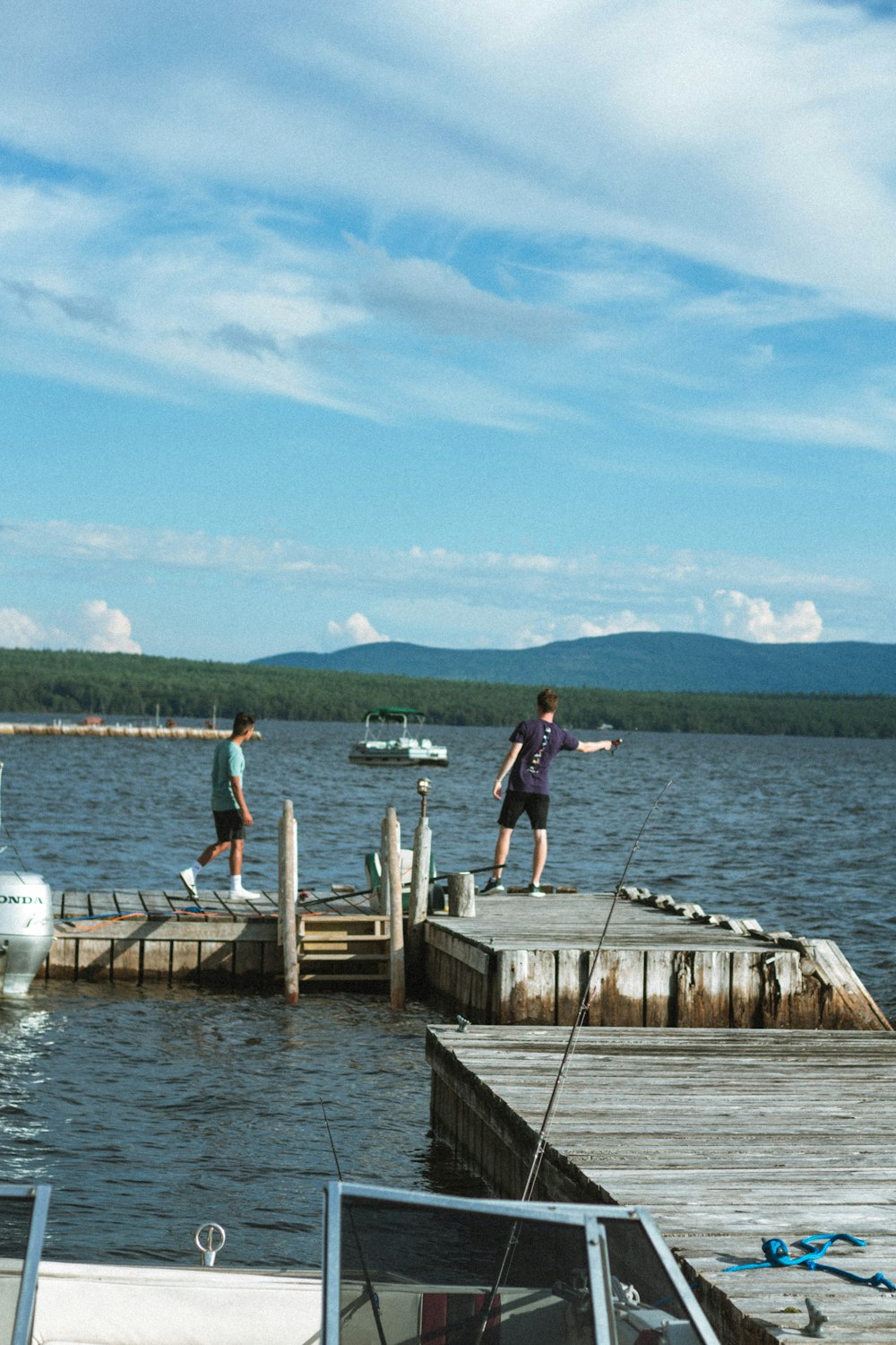 man in white t-shirt and black pants standing on brown wooden dock during daytime