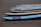 Several surfboards are neatly lined up on a sandy beach, with their noses pointing in the same direction. The boards vary slightly in color and design, predominantly featuring shades of blue, white, and a touch of yellow.