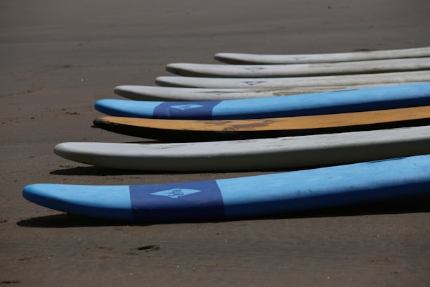 Close-up of surfboards lined up on the sandy beach with footprints leading to the water.
