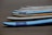 Several surfboards are neatly lined up on a sandy beach, with their noses pointing in the same direction. The boards vary slightly in color and design, predominantly featuring shades of blue, white, and a touch of yellow.