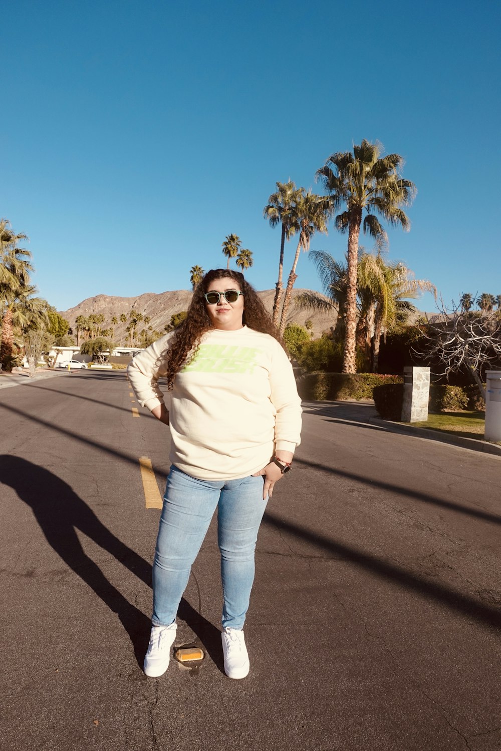 woman in white long sleeve shirt and blue denim jeans standing on gray asphalt road during