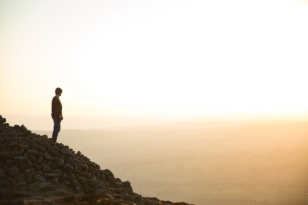 silhouette of man standing on rocky hill during daytime