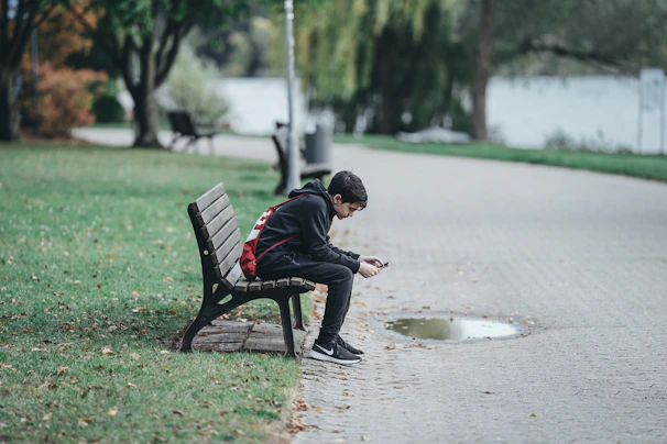 A candid moment of a young person scrolling through social media on a sunny park bench.