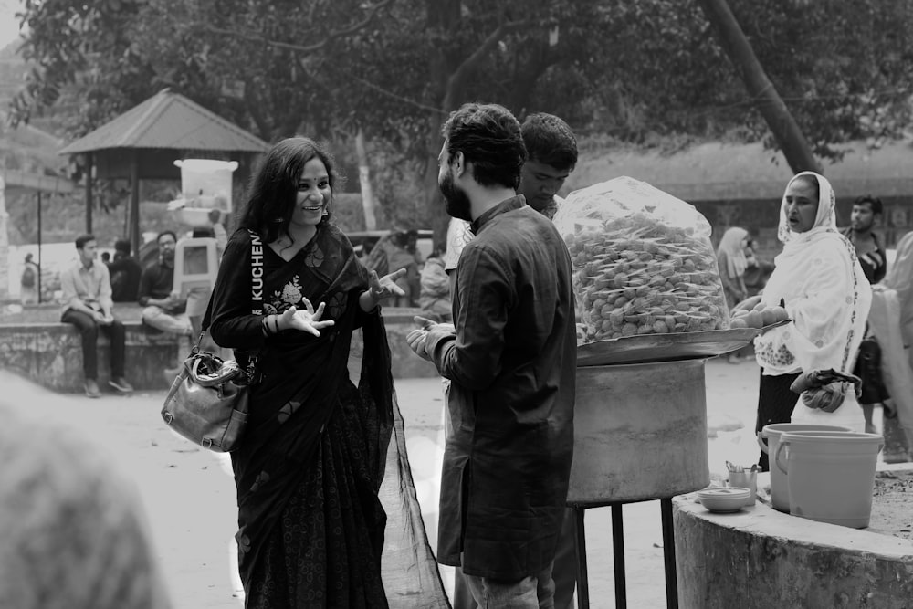 grayscale photo of woman in black dress standing beside man in black coat