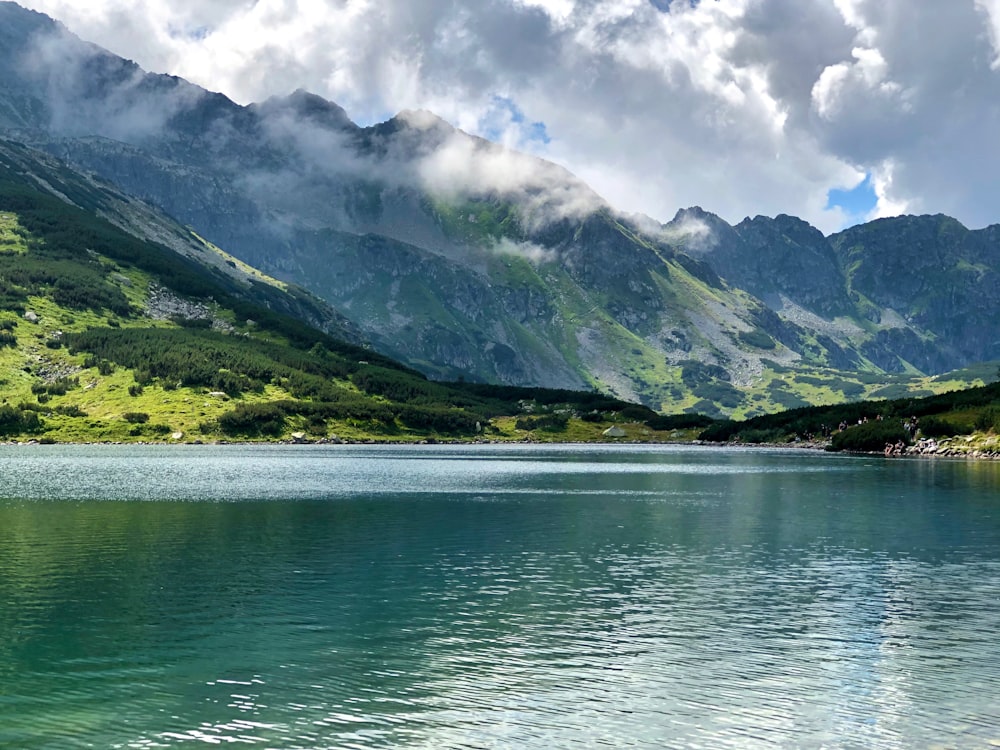 Grüner und grauer Berg neben Gewässer unter blau-weißem bewölktem Himmel tagsüber