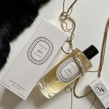 An elegantly arranged display of luxury fragrance items, featuring a large bottle of perfume with a black cap, a matching rectangular box, and a smaller box. The items are adorned with a golden chain draped artfully around them, set against a contrasting background with a patch of black fabric.