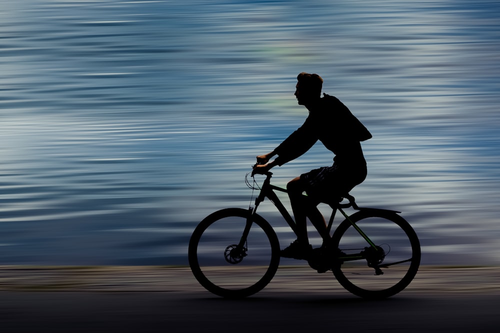 낮 동안 해변에서 자전거를 타는 검은 재킷을 입은 남자