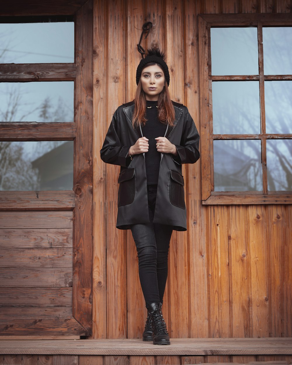 woman in black coat standing near brown wooden window