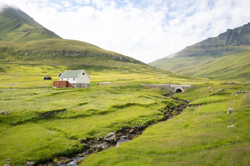 white wooden house on green grass field near mountain under white clouds during daytime