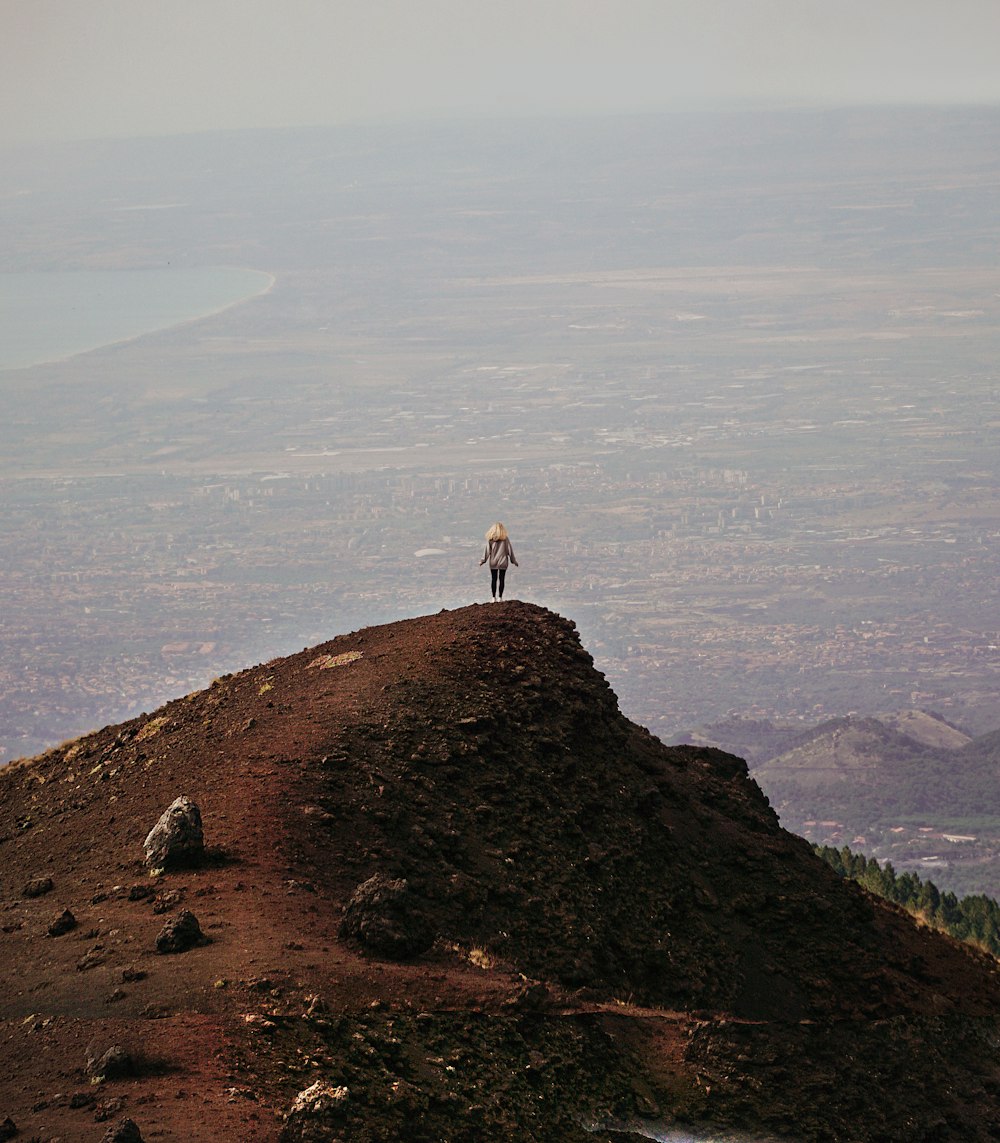 pessoa na camisa branca em pé na formação rochosa marrom durante o dia