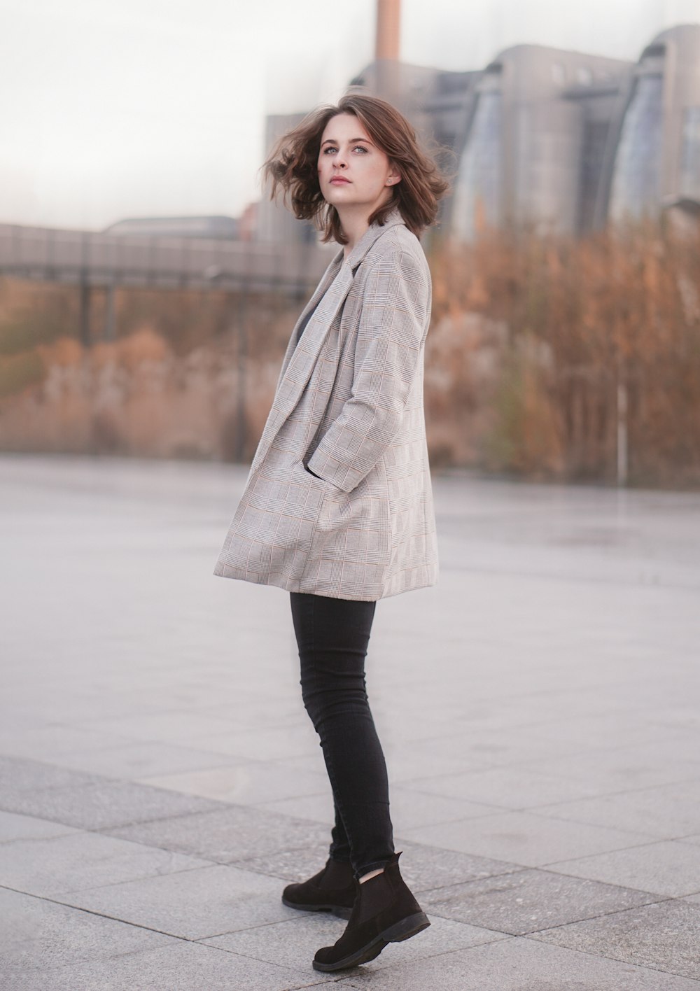 woman in gray coat and black leggings standing on gray concrete floor during daytime