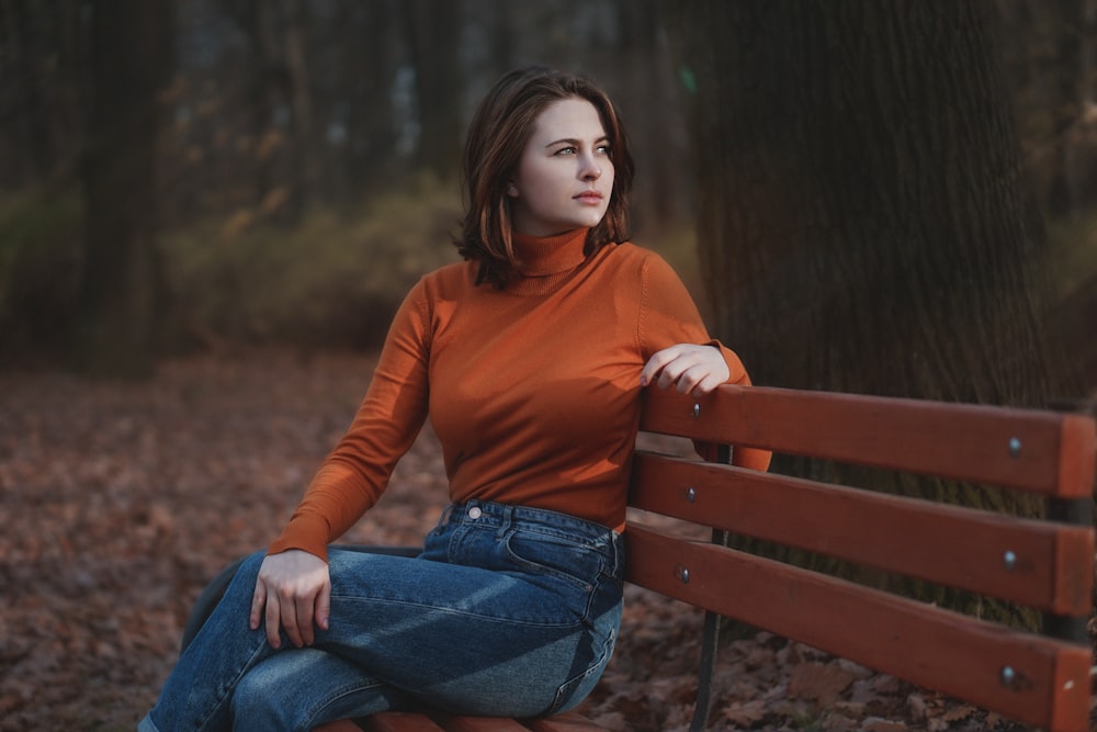 woman in red long sleeve shirt and blue denim jeans sitting on brown wooden bench