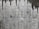 A textured concrete wall with dark water stains creating irregular patterns that resemble icicles or stalactites. The wall's surface features various shades of gray with a rough, aged appearance.