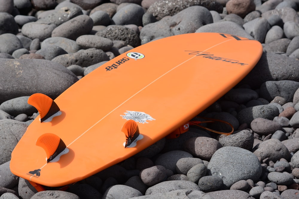 Tabla de surf naranja sobre piedras grises