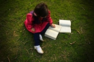 A child sitting on a soft blanket outdoors, deeply engaged in reading a Tiny Farm Press book.