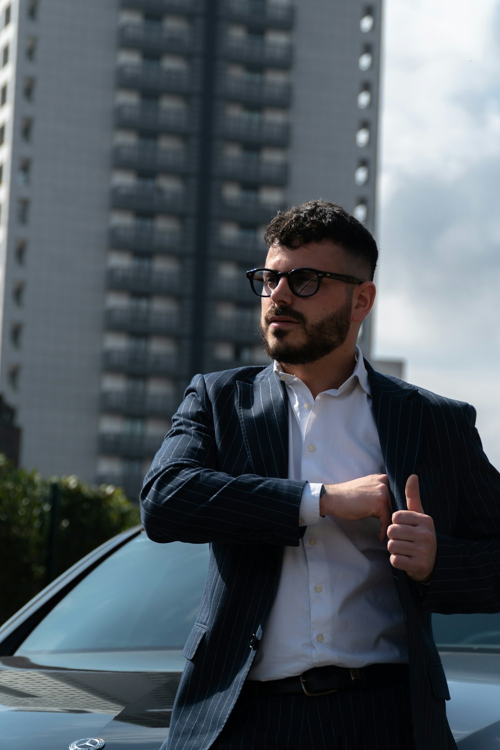 man in black suit jacket and white dress shirt standing beside black car during daytime