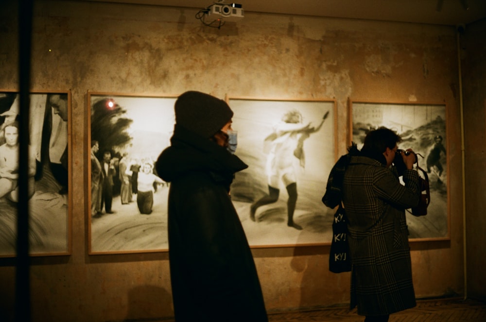 man in black coat standing in front of painting