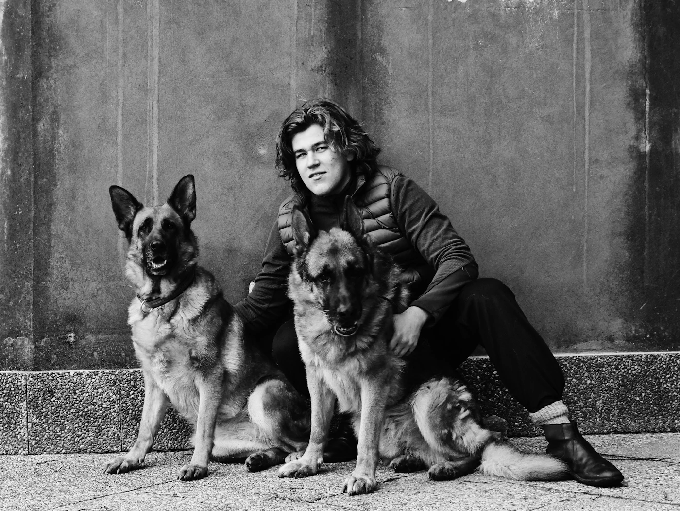A man and a woman standing close together with a German Shepherd between them in a quiet black and white photo