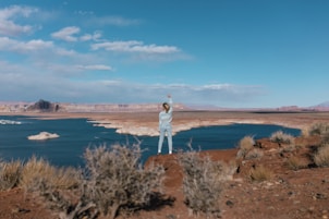 woman in white long sleeve shirt standing on brown grass field near body of water during