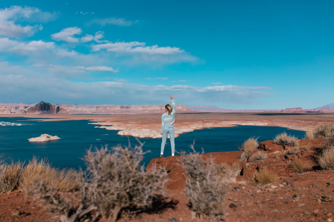 woman in white long sleeve shirt standing on brown grass field near body of water during