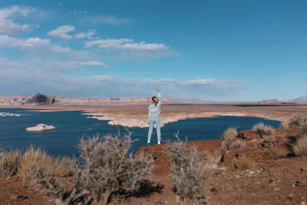 woman in white long sleeve shirt standing on brown grass field near body of water during