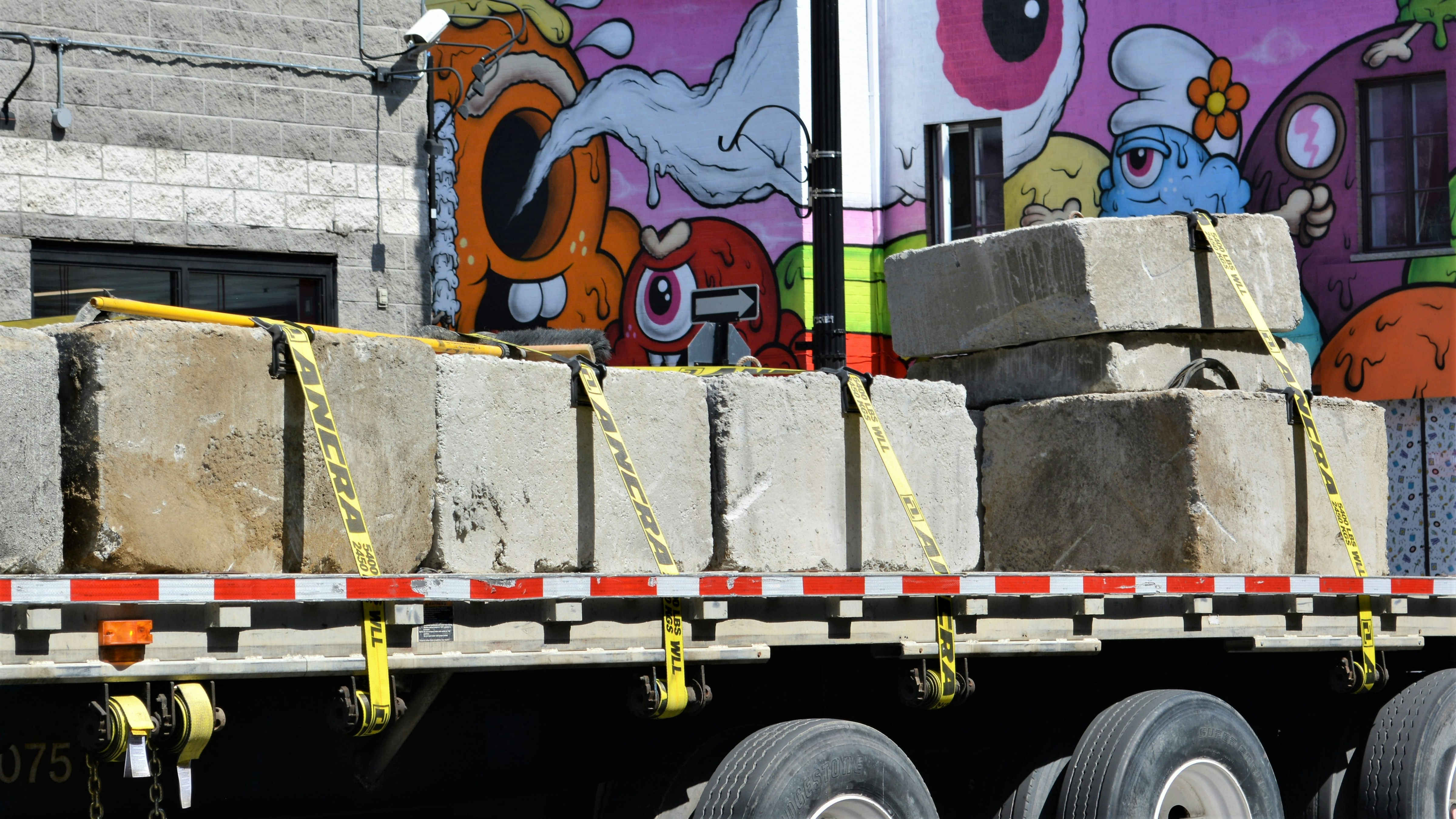 Flatbed truck with construction equipment secured with straps, highway setting